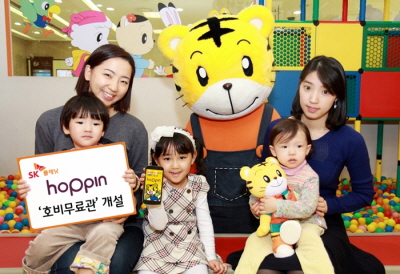 왼쪽 모델이 SK플래닛,_호핀 호비무료관 개설이라고 적힌 배너를 들고 있고 다른 모델들은 호비 캐릭터 인형과 함께 포즈를 취하고 있습니다.