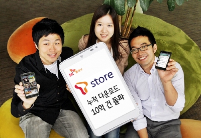 핸드폰에 삽입된 이미지에 SK플래닛 ‘T스토어’, 누적 다운로드 10억 건 돌파라고 적혀있습니다. 각 모델들은 핸드폰으로 앱 구동화면을 보여주고 있습니다.