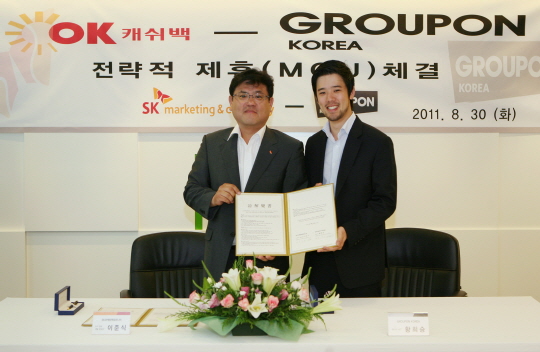 SK마케팅앤컴퍼니-그루폰코리아 MOU 기념사진입니다. 현수막에 OK캐쉬백 그루폰 코리아 전략적 제휴 체결이라고 적혀있습니다.
