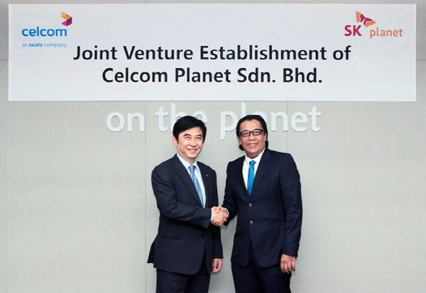 SK플래닛-셀콤 악시아타, e-커머스 사업 추진을 위한 합작법인 설립 홍보사진입니다. 관계자들이 기념사진을 촬영하고 있습니다. 그리고 뒤쪽 현수막에는 Celcom과 SK planet이라고 적혀 있으며 Joint Venture Establishment of Celcom Planet Sdn.Bhd.라고 적혀있습니다.