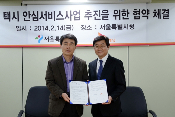 서울시-SK플래닛,택시 안심귀가 서비스 업무 협약 체결 관련 홍보 사진입니다. 각 관계자들이 기념사진을 촬영하고 있습니다. 현수막에는 택시 안심서비스사업 추진을 위한 협약 체결이라는 글과 일시 및 장소가 삽입되어 있습니다.