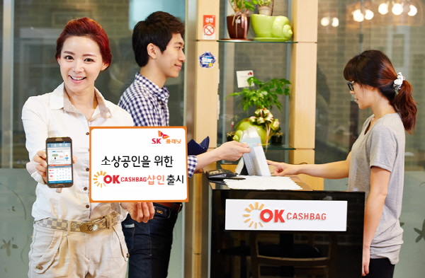 SK플래닛, 소상공인을 위한 상생의 모바일 마케팅 플랫폼 OK캐쉬백 샵인 출시 관련 홍보 사진입니다. 왼쪽 모델은 소상공인을 위한 OK캐쉬백 샵인 출시라고 적힌 배너를 들고 있고 오른쪽 모델은 사용하는 방법을 시연하고 있습니다.