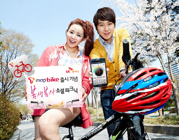 SK플래닛, ‘T맵 바이크’ 앱 출시 홍보 사진입니다. 왼쪽 모델은 T맵 바이크 출시기념 봄생봄사 소셜 피크닉이라고 적힌 배너를 들고 있고 오른쪽 모델은 휴대폰으로 앱 구동화면을 보여주고 있습니다.