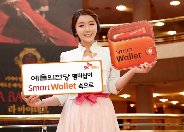 SK플래닛 스마트월렛,예술의전당 모바일 멤버십 제공 한다는 홍보 사진입니다. 모델이 왼손에는 예술의전당 멤버십이 스마트 월렛 속으로라고 적힌 배너를 들고 있고 오른손에는 앱 아이콘을 들고 있습니다.